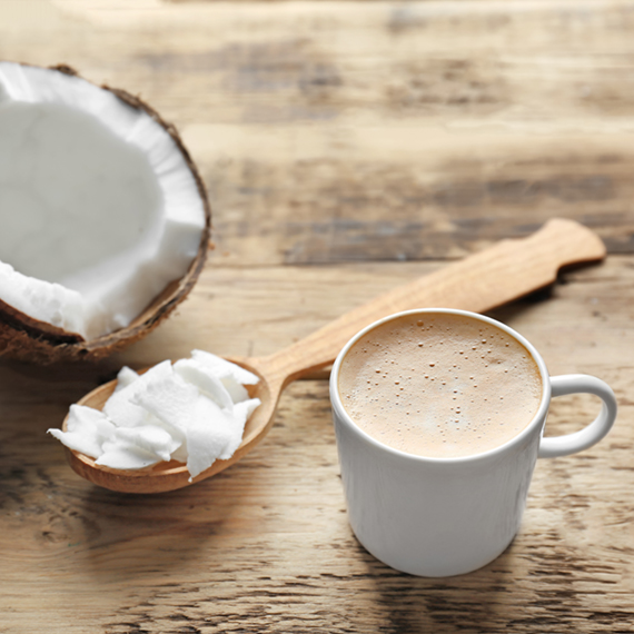 Cup of tasty coconut coffee and spoon with butter on wooden table