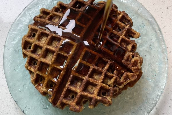 A waffle on a glass plate with syrup being poured