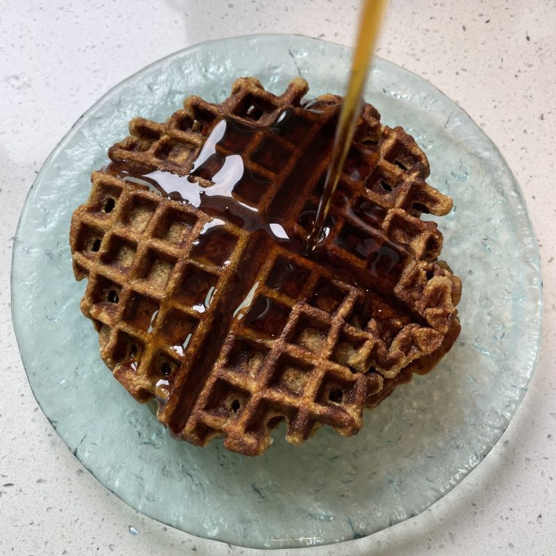 A waffle on a glass plate with syrup being poured