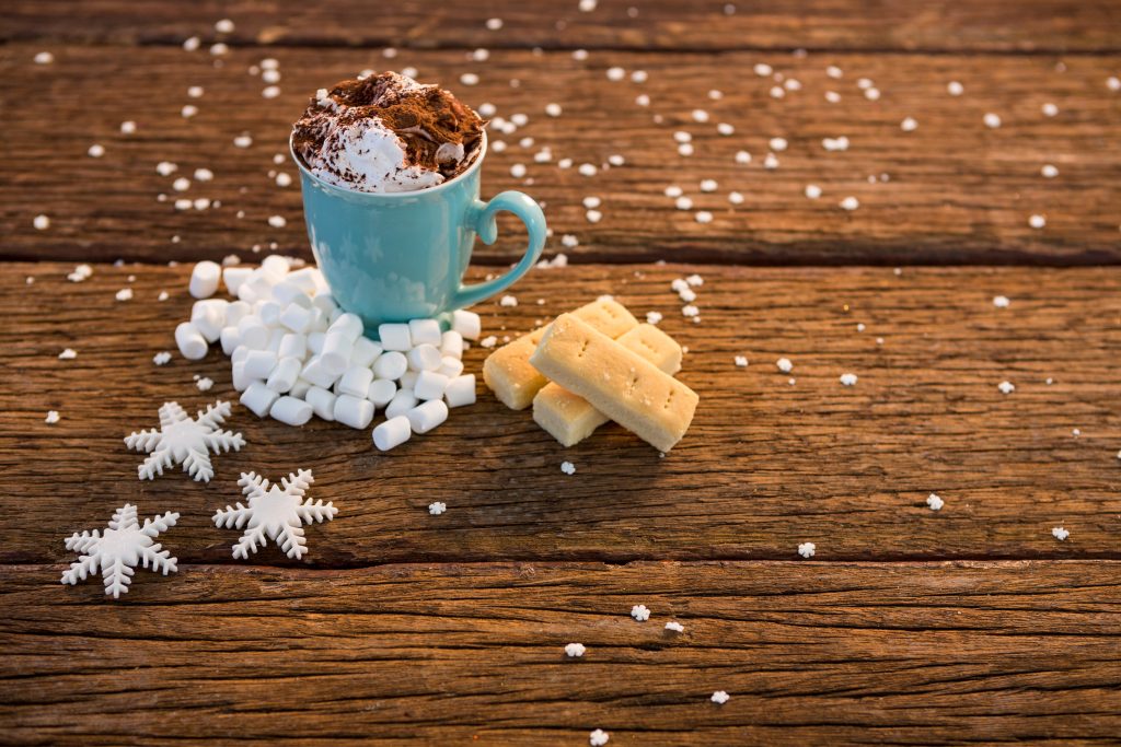 Cup of coffee with snowflake and marshmallow on wooden plank