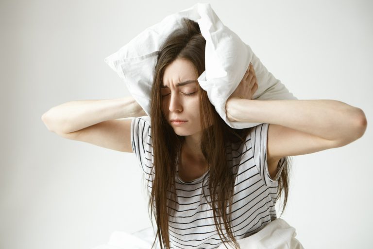 Young tired woman holding a pillow over her ears