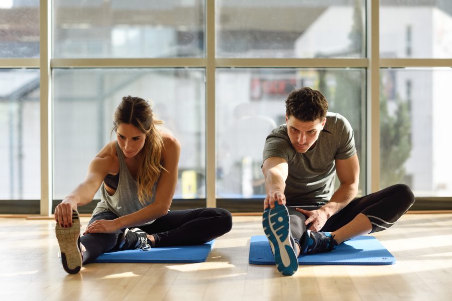 Two people stretching their legs in gym.