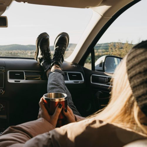 Woman riding in a car with her feet on dash holding a travel mug