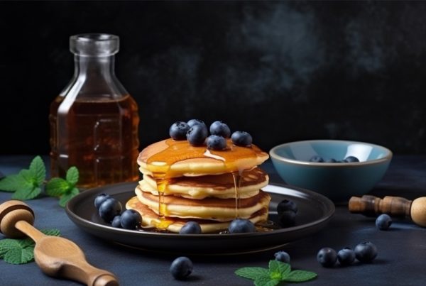 Pancakes on a plate with blueberries on top and a bottle of honey behind them