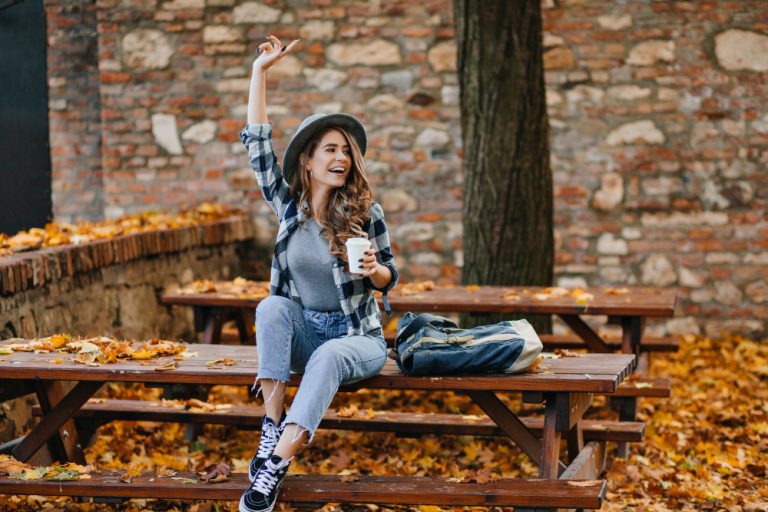 Young, happy woman with a cup of coffee on a park bench in the fall