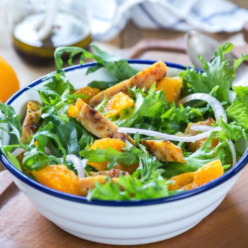 Grilled chicken salad with orange slices in a white bowl on a table