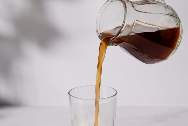 Pouring iced coffee from a glass pitcher into a clear glass