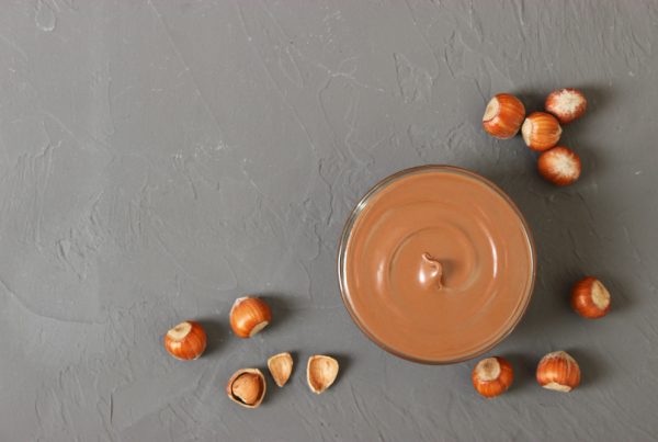 Raw hazelnuts on a counter with a glass of hazelnut paste