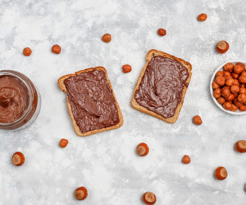 Toast on a marble counter with hazelnuts and chocolate spread in a glass jar