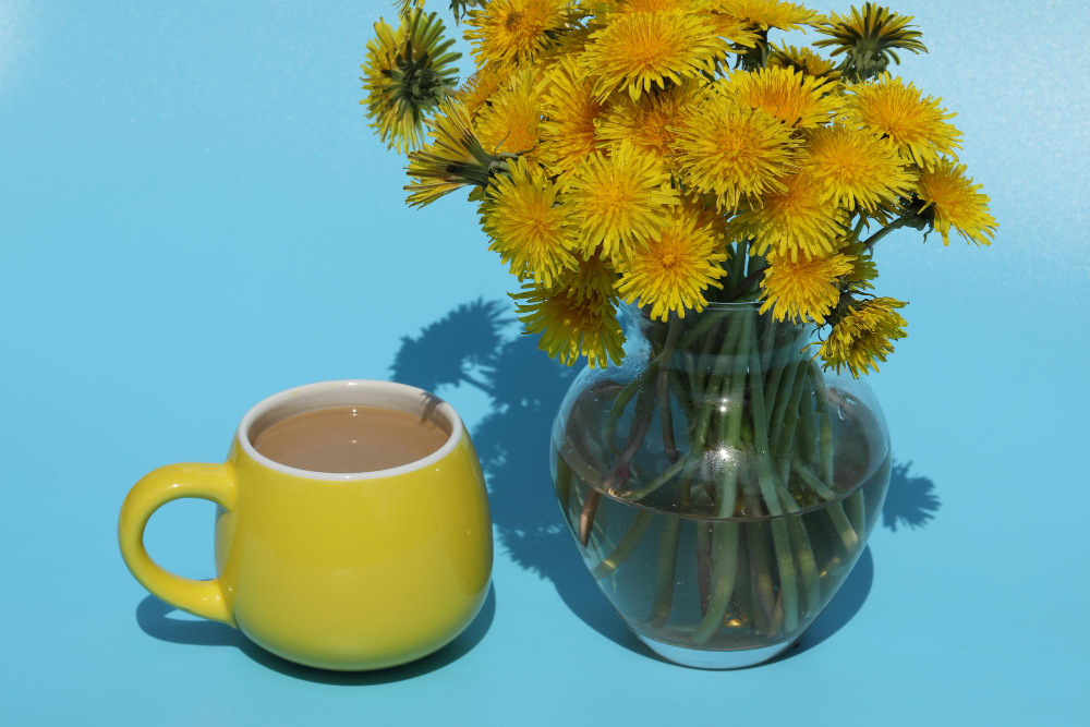 cup of coffee next to a dandelion bouquet in a clear vase