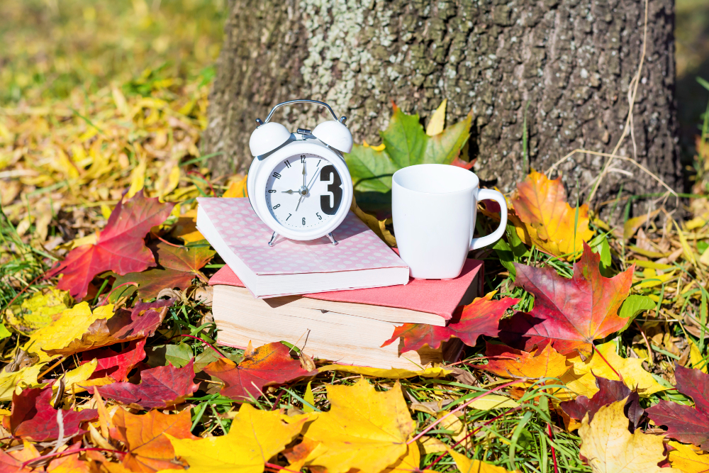 Clock and coffee cup sitting in fall leaves outside next to a tree