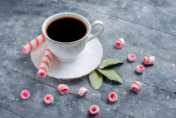 Cup of coffee hot and strong along with pink stick candies on grey, coffee candy sweet drink