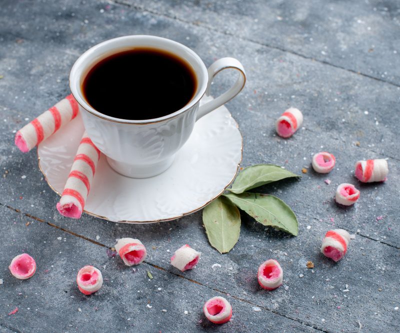 Cup of coffee hot and strong along with pink stick candies on grey, coffee candy sweet drink