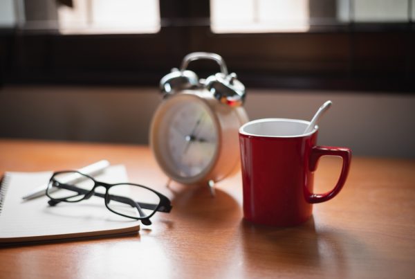 Alarm clock on a table with coffee cup and reading glasses