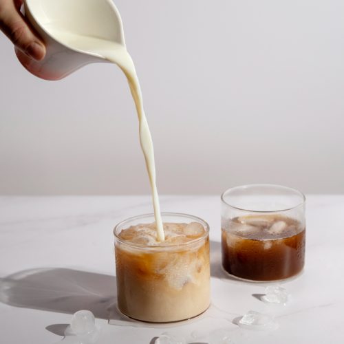Pouring cream into a clear glass of iced coffee