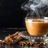Steaming cup of caffeine free chai on black counter with anise and cinnamon sticks