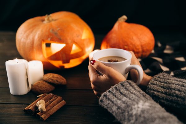 Woman holding hot cocoa in front of jack-o-lanterns