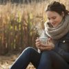 A woman sitting outside in a field in fall drinking a hot cup of coffee