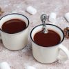 2 white mugs with hot chocolate on a table and some marshmallows