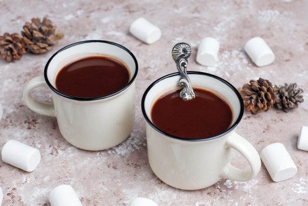 2 white mugs with hot chocolate on a table and some marshmallows