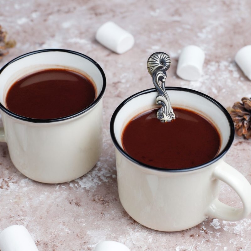 2 white mugs with hot chocolate on a table and some marshmallows