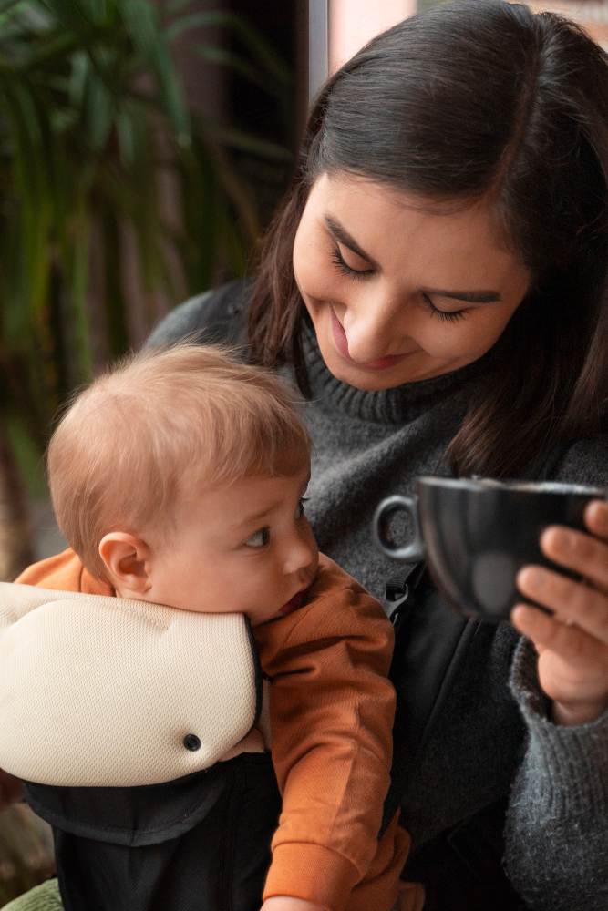 mom holding a baby in a front carrier while having coffee