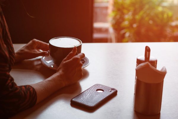 Someone sitting at a table with a cup of coffee and cell phone face down