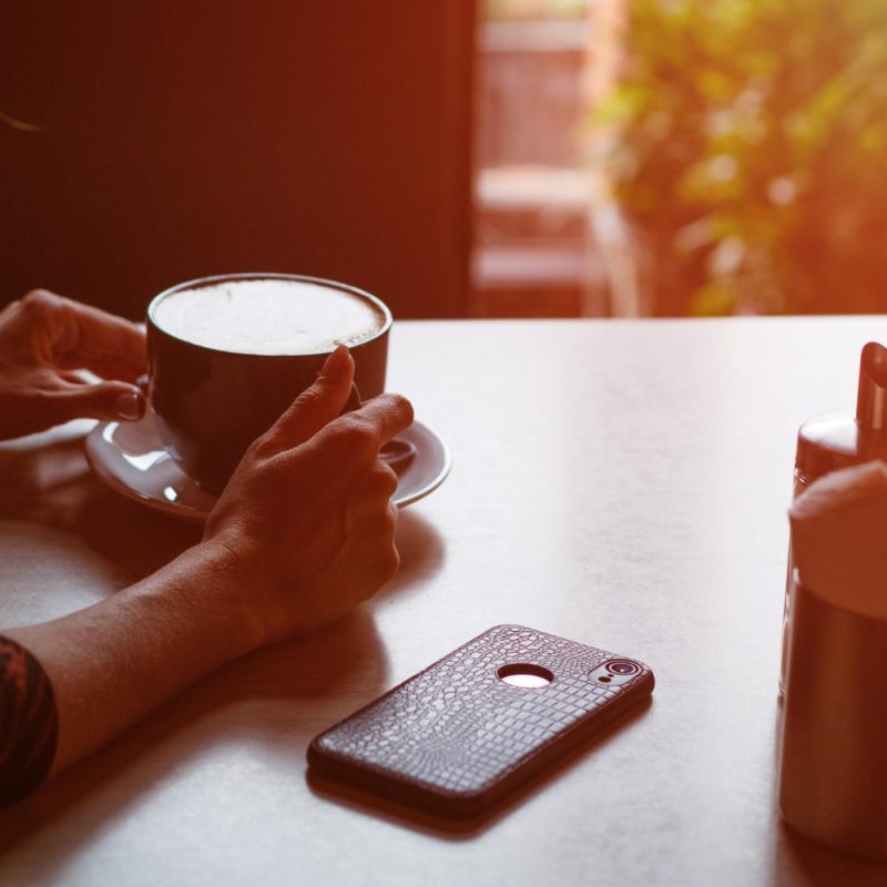 Someone sitting at a table with a cup of coffee and cell phone face down