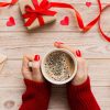 Woman's hands holding a coffee cup on a table with red ribbon and red hearts on packages