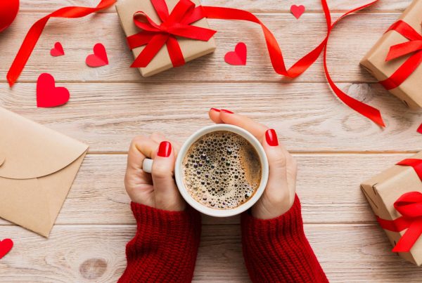 Woman's hands holding a coffee cup on a table with red ribbon and red hearts on packages