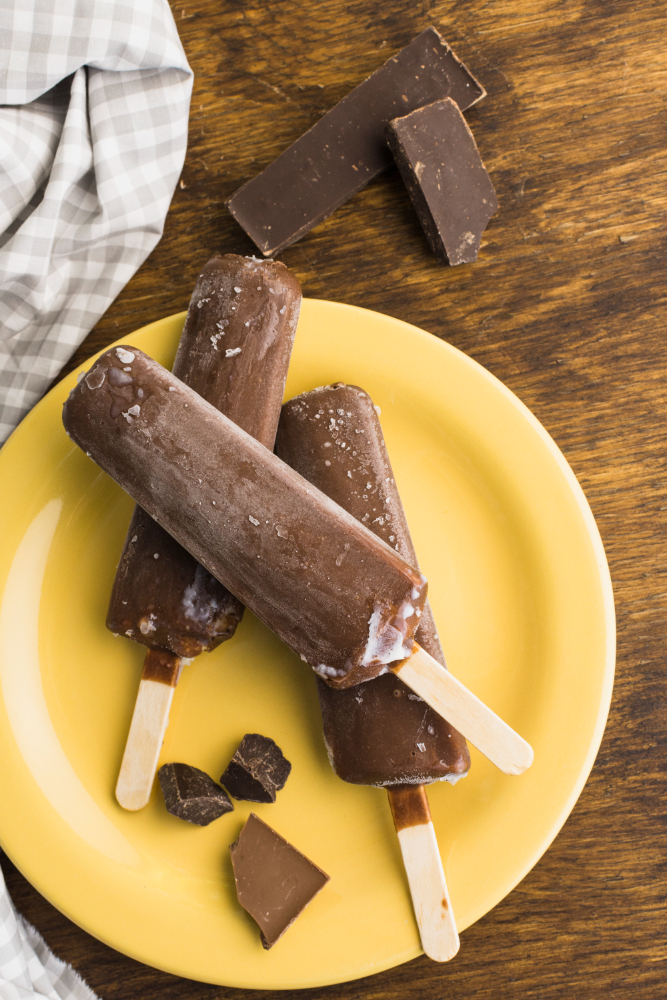 3 fudgesicles on a yellow plate with some bars of chocolate