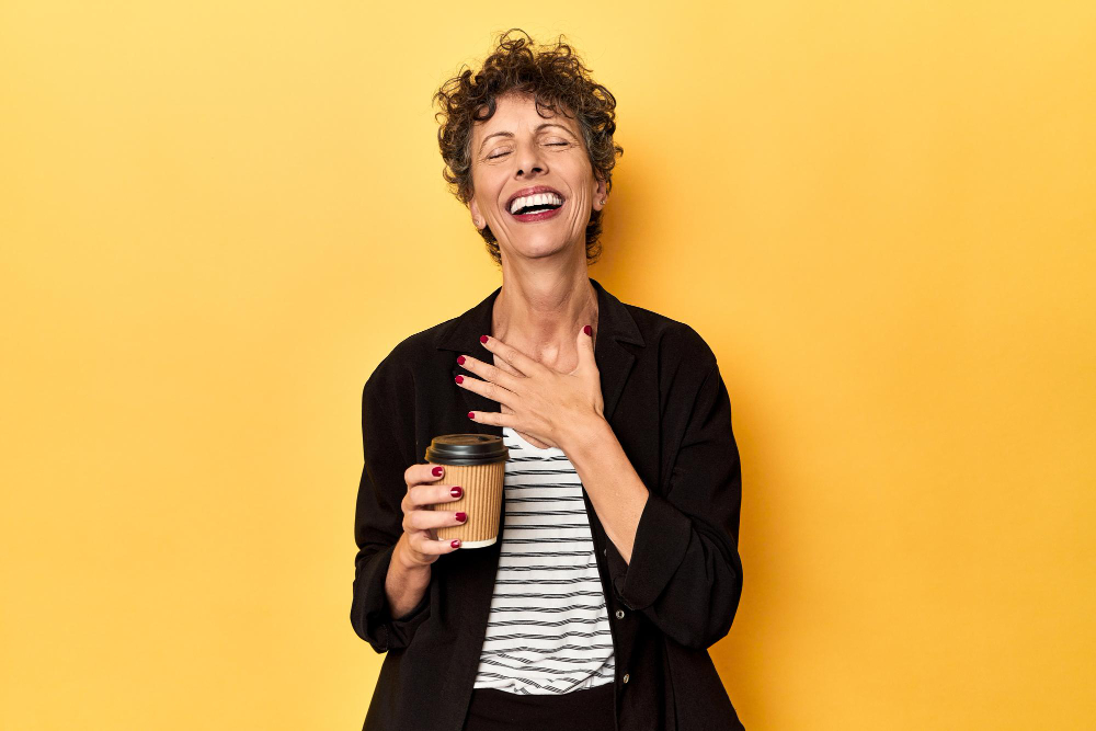 Laughing woman holding a to-go cup with a yellow background
