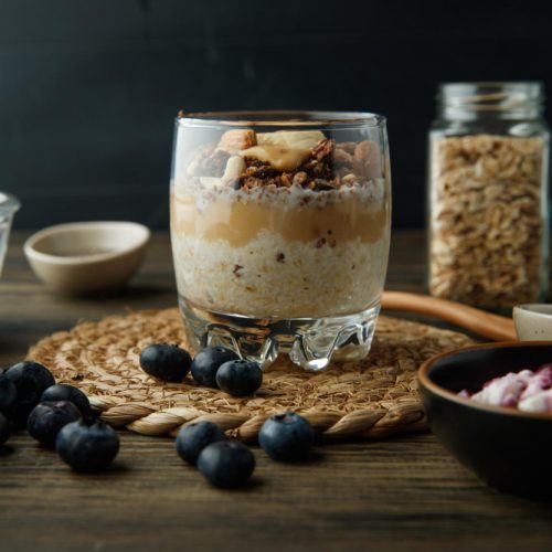 Acear glass on a wood table with overnight oats and blueberries