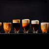 A line of coffees in clear glasses in front of a black background with varying shades of milk