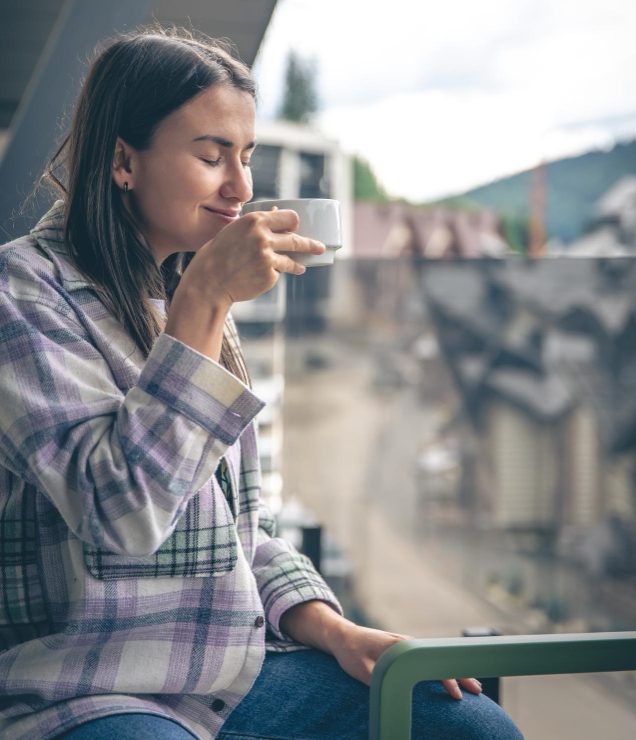 A women in a plaid shirt enjoying morning coffee on a balcony