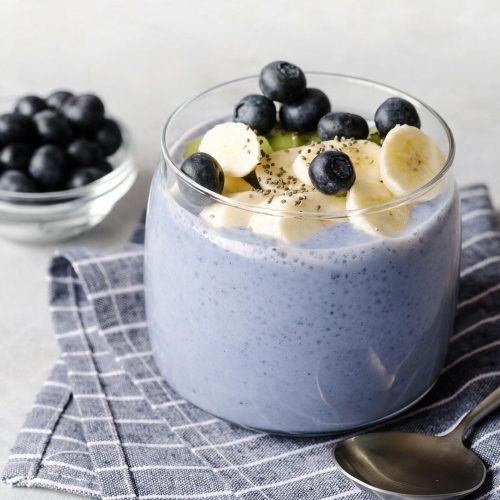 Blueberry chia seed pudding in a clear glass with blueberries and bananas slices on a blue pinstriped napkin