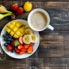 A cup of coffee with fresh fruit on a white plate on a wood table