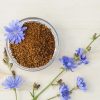 dried chicory root in a clear bowl with chicory flowers on a table