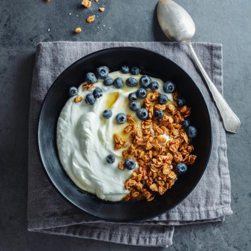 A bowl of yogurt with granola and blueberries on a gray table