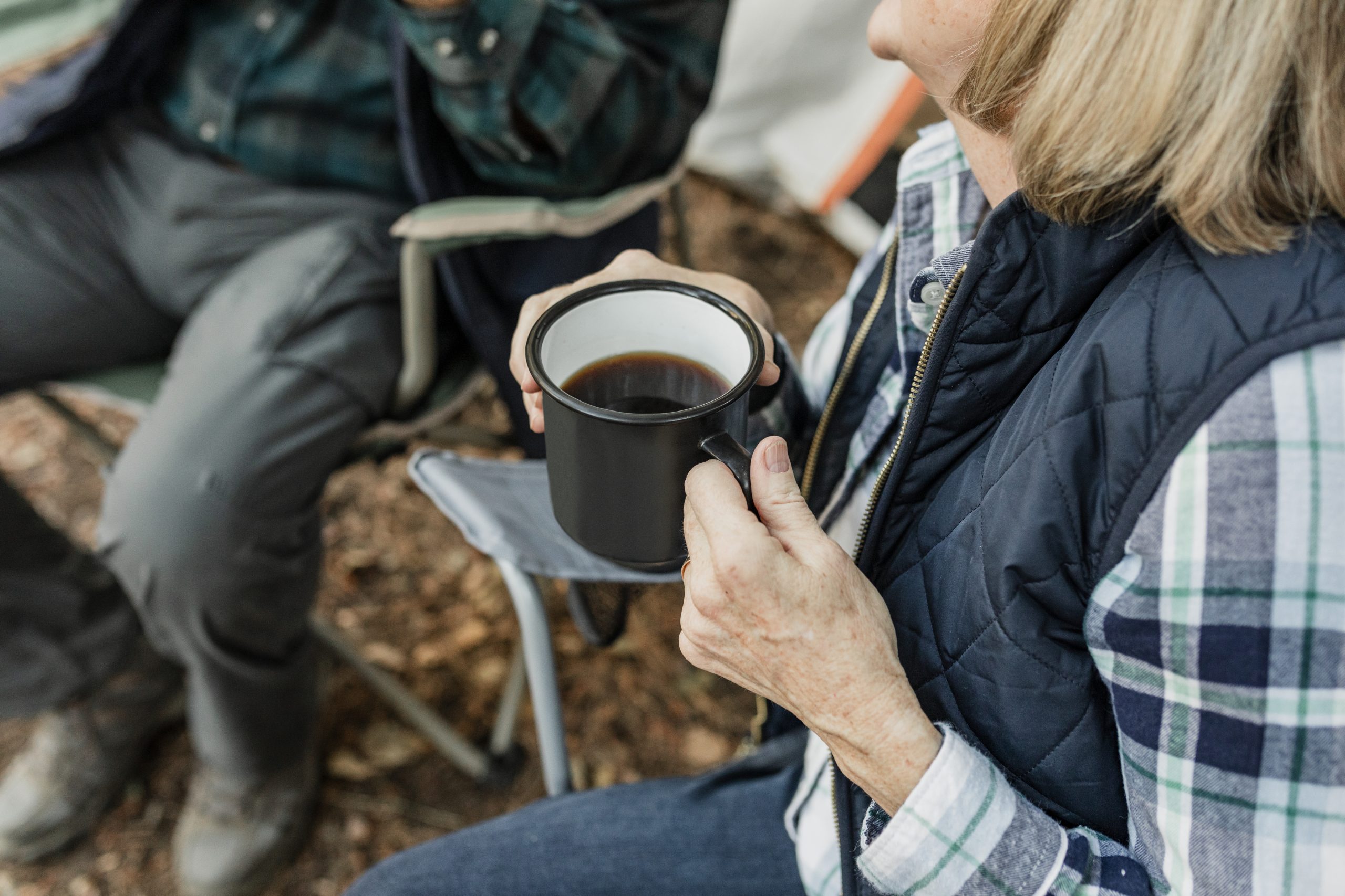 Happy retired couple having coffee by the tent in the forest